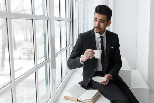 Σκέψης επιχειρηματία στο κοστούμι που κάθεται στο περβάζι και ποτά καφέ. — Φωτογραφία Αρχείου
