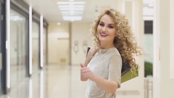 Hermosa mujer dando la vuelta y mostrando los pulgares hacia arriba con bolsas de compras en el centro comercial, cámara lenta . — Vídeo de stock