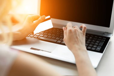 Kredi kartı tutan ve güneş ışığı altında dizüstü bilgisayar kullanarak eller.