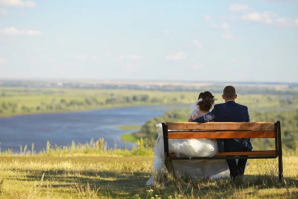 Jeune couple romantique de mariage assis sur un banc en bois en plein air sur fond de rivière . — Photo