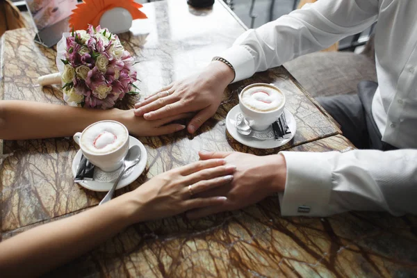Para ślub w kawiarni. Człowiek posiada rękę, pije cappuccino. Przerwa na kawę narzeczeni randki prezent, bukiet na stół — Zdjęcie stockowe