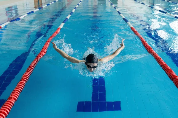 Jeune fille en lunettes et bonnet de natation style coup de papillon dans la piscine d'eau bleue . — Photo