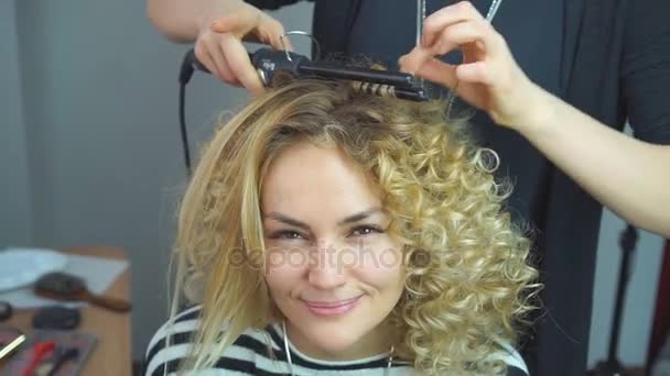 Friseurin macht Frisur zu blonden Mädchen im Schönheitssalon. Stylistin macht afrikanische Locken im Schönheitssalon. — Stockvideo