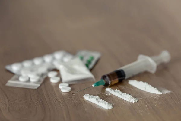 Líneas y paquetes plásticos de cocaína u otras drogas. polvo blanco narcótico y jeringa en la mesa de madera . — Foto de Stock