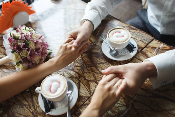 Para ślub w kawiarni. Człowiek posiada rękę, pije cappuccino. Przerwa na kawę narzeczeni randki prezent, bukiet na stół — Zdjęcie stockowe