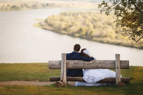 Jeune couple romantique de mariage assis sur un banc en bois en plein air sur fond naturel — Photo