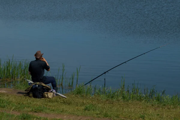Рыбак с удочкой ловит рыбу, сидя на берегу реки — стоковое фото