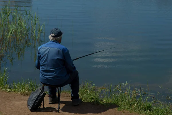 Рыбак с удочкой ловит рыбу, сидя на берегу реки . — стоковое фото
