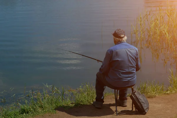 Рыбак с удочкой ловит рыбу, сидит на берегу реки. солнце — стоковое фото