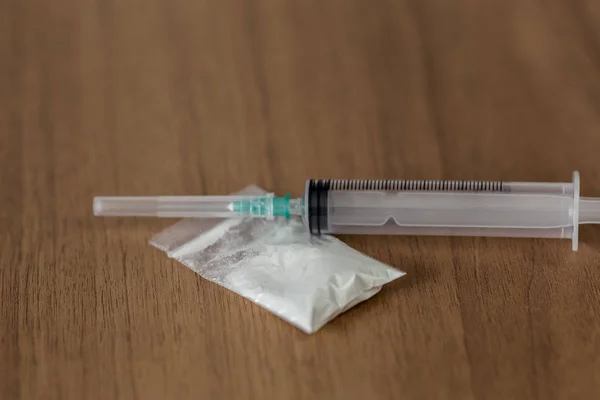 Paquet plastique avec cocaïne et seringue sur la table en bois — Photo