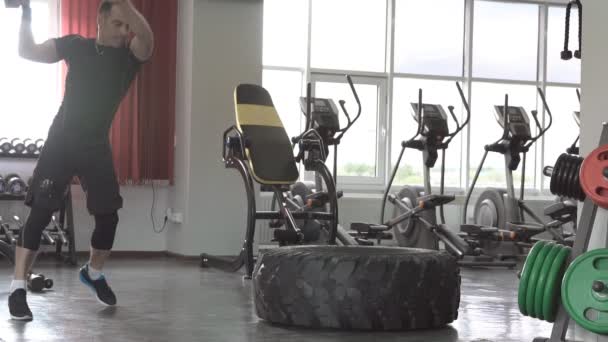 Медленное движение мужской тренировочной модели фитнес-тренировки с тяжелыми и большими шинами и молотком в фитнес-центре — стоковое видео