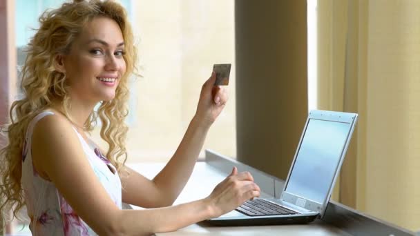 Hermosa mujer que sostiene la tarjeta de crédito en la mano e ingresa el código de seguridad utilizando el teclado portátil — Vídeo de stock