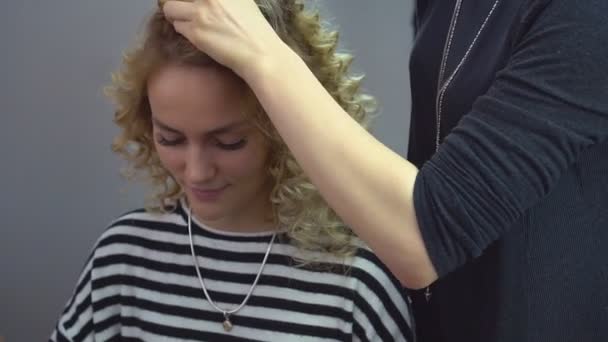 Belle fille blonde aux cheveux longs, coiffeuse fait des boucles africaines dans un salon de beauté. Soins capillaires professionnels et création de coiffures . — Video