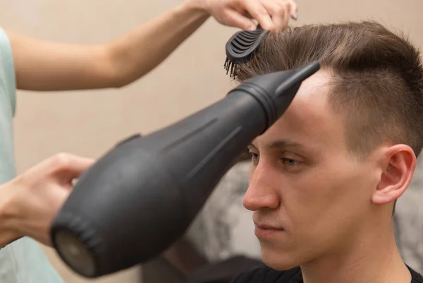 Жіночий перукар сушить волосся свого чоловічого клієнта в перукарні — стокове фото