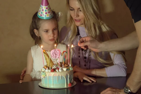 Madre e hija cuentan velas Ing en un pastel de cumpleaños. niña en un sombrero festivo en una fiesta para niños — Foto de Stock