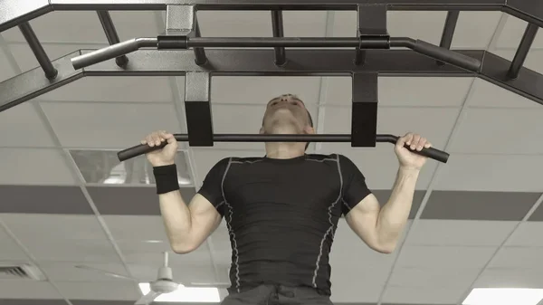 Atleta muscular fitness modelo masculino puxando para cima na barra horizontal em um ginásio. — Fotografia de Stock