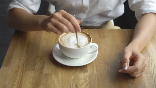 Die Hände der Mädchen rühren den Zucker in einer Tasse Latte in Großaufnahme — Stockvideo