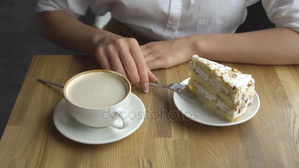 Una ragazza beve caffè e mangia una torta dolce in un caffè. Primo piano mani femminili — Video Stock