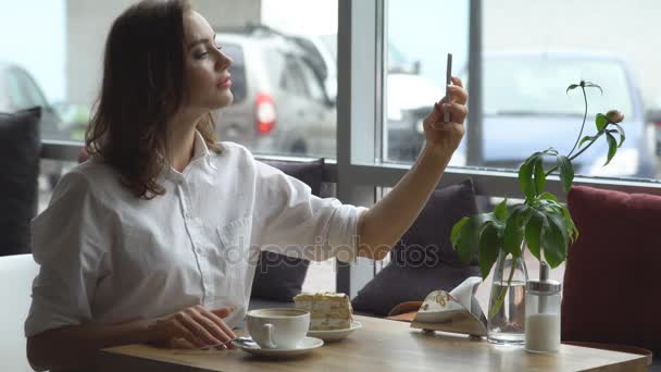 Giovane bella ragazza facendo selfie sulla fotocamera smartphone seduto in accogliente caffè — Video Stock