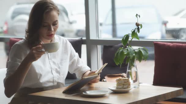 Девушка читает книгу и отдыхает в кафе. девушка в деловой одежде отдыхает во время обеденного перерыва — стоковое видео