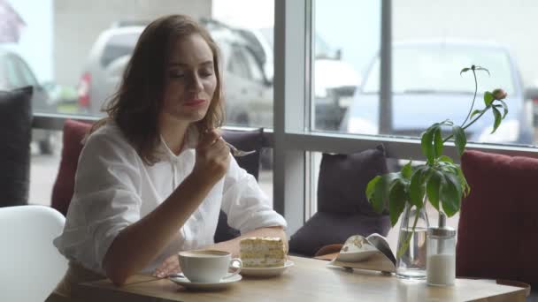 La chica disfruta de un café fragante y pastel dulce sentado en un café. Mujer de negocios descansando durante el descanso — Vídeo de stock