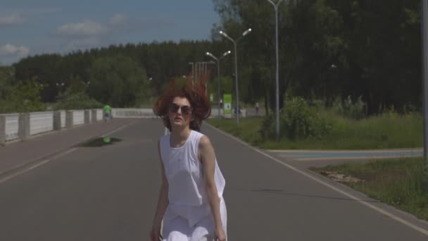 Безтурботна молода дівчина стрибає і розважається в літньому парку. Приваблива дівчина в сонцезахисних окулярах і біла сукня, що йде на відкритому повітрі. Повільний рух — стокове відео