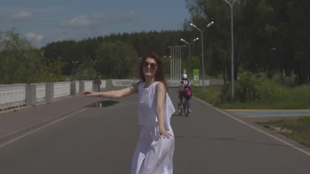 평온한 어린 소녀 점프 하 고 여름 공원에서 재미. 선글라스와 야외에서 걷고 흰색 드레스에 매력적인 여자. — 비디오