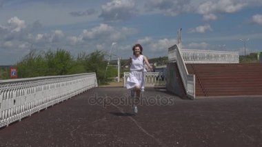 Mutlu genç kız atlama ve yaz parkta eğleniyor. Çekici kız güneş gözlüğü ve açık havada yürüyüş beyaz bir elbise. Ağır çekim