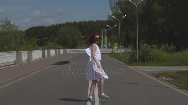 Ung vacker flicka i solglasögon och en vit klänning som promenader utomhus — Stockvideo