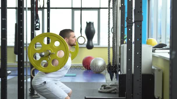 Styrketräning i gymmet. killen gör knäböj med en skivstång. bodybuilder gör träning med skivstång. sidovy — Stockvideo