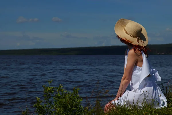 Žena v bílých šatech a klobouk relaxovat na riverside — Stock fotografie