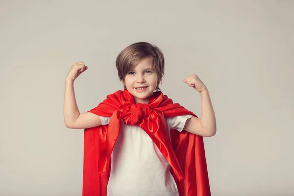 Linda niña supermujer en capa roja muestra su músculo — Foto de Stock