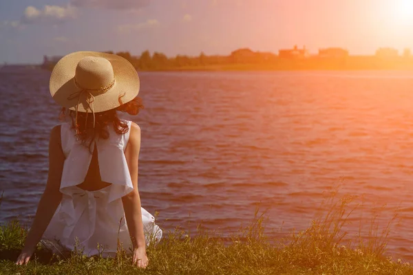 Žena v bílých šatech sedí na riverside, zpět zobrazení — Stock fotografie