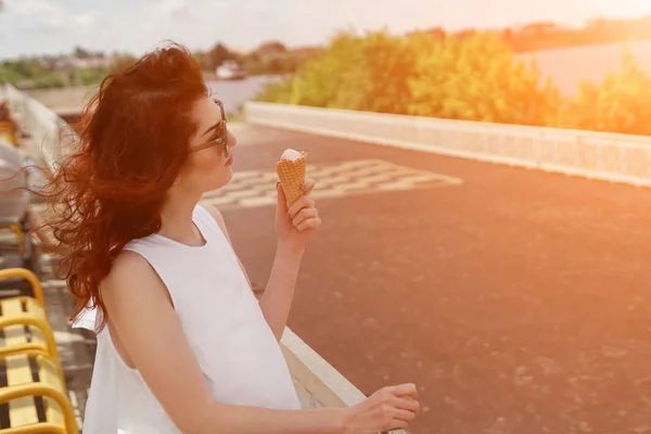 Женщина в солнечных очках ест мороженое на берегу реки — стоковое фото