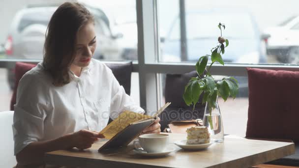 Девушка читает книгу и отдыхает в кафе. девушка в деловой одежде отдыхает во время обеденного перерыва — стоковое видео