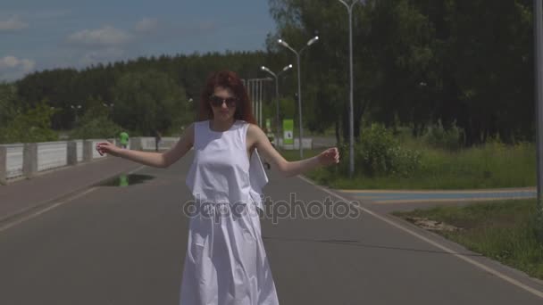 Jovem despreocupada pulando e se divertindo no parque de verão. Menina atraente em óculos de sol e um vestido branco andando ao ar livre. Movimento lento — Vídeo de Stock
