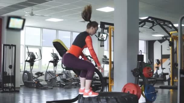 Atletische meisje springen op een grote trekker-wiel. — Stockvideo