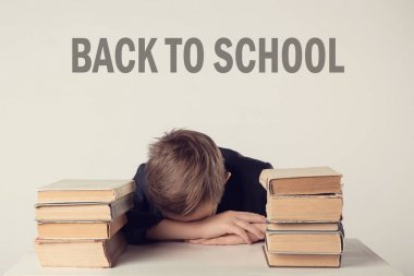 Pupil in suit at his desk on grey background with books. Boy fell asleep during homework. Inscription 'Back to School'.