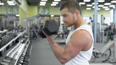 spor salonunda dumbbells ile egzersiz yaparak genç kaslı adam. Spor egzersiz, erkek vücut geliştirmeci portresi
