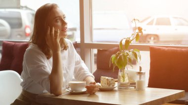 bir kız bir kafede oturan bir cep telefonu kullanır. genç bir kadının cep telefonu ve içme kahve içeren bir ileti gönderir