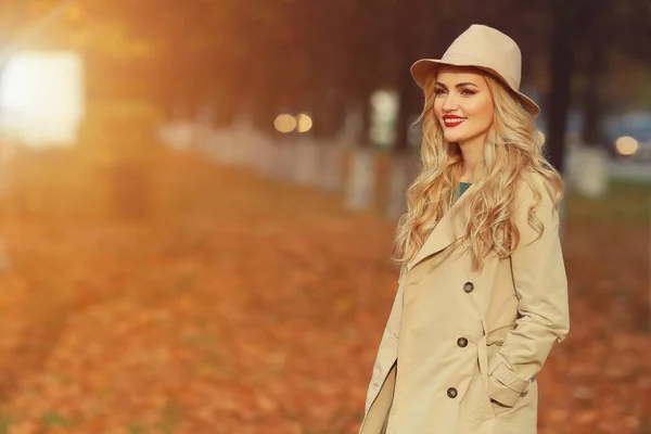 Bella donna elegante in piedi in cappello beige alla moda in un parco in autunno. Copyspace, luce del sole — Foto Stock