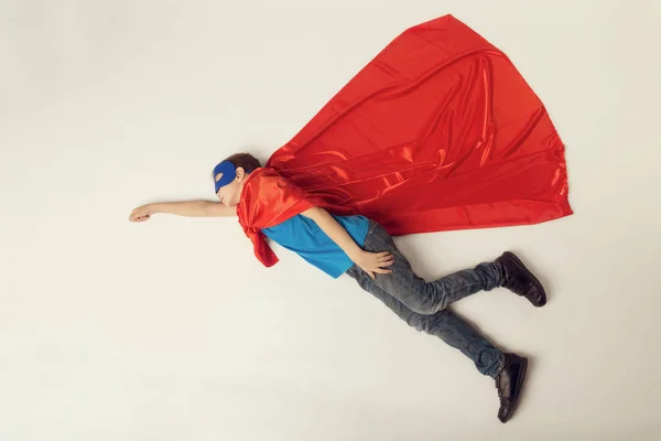 Chico superhéroe volando. Super héroe niño en capa roja y máscara azul. espacio de copia, tonificado — Foto de Stock