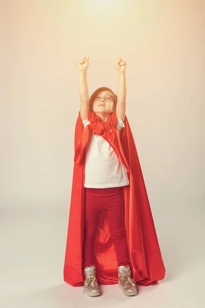 Superhéroe niña en capa roja levantó las manos — Foto de Stock