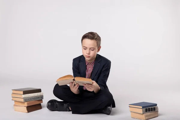 Niño lindo en un traje sentado y sosteniendo un libro sobre un fondo blanco — Foto de Stock