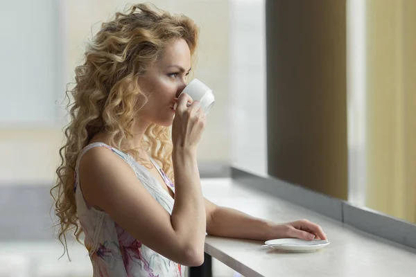 Gyönyörű szőke lány iszik egy csésze forró kávé vagy tea a kávézóban — Stock Fotó