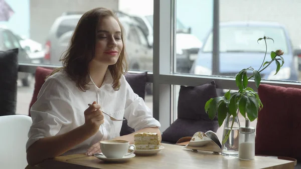 Joven hermosa hembra disfruta de un café fragante y pastel dulce sentado en la cafetería. Mujer de negocios descansando durante el descanso —  Fotos de Stock