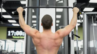 Atlet egzersizleri sırt kasları için yapar. Kaslı vücut geliştirmeci salonunda blok aygıtları üzerinde arka