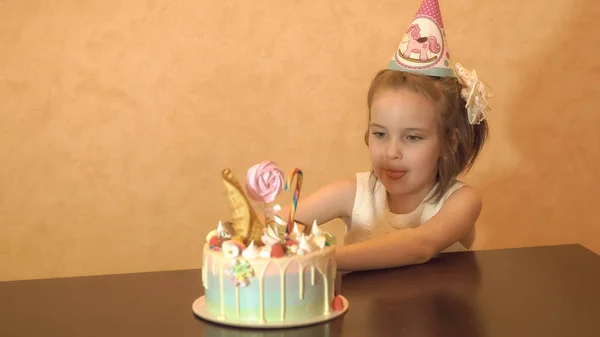 Fiesta de cumpleaños de los niños. Niña mirando el pastel y lamiendo. celebración familiar . —  Fotos de Stock
