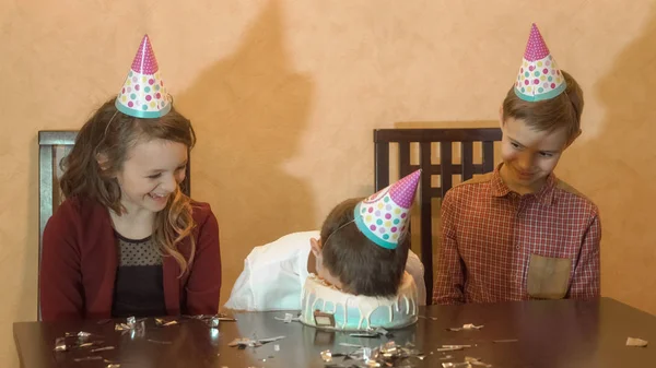 誕生日パーティーで屈託のない子どもたち。少年は、バースデー ケーキに顔をダンク シュート。家族のお祝いのコンセプト. — ストック写真