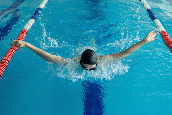 Jeune femme en lunettes et bonnet de natation style coup de papillon dans la piscine intérieure de course d'eau bleue — Photo